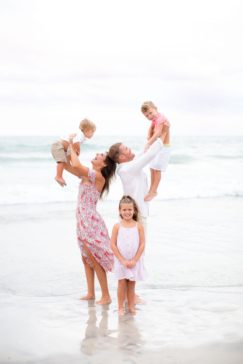 Family enjoying a playful moment together at the beach with waves in the background.