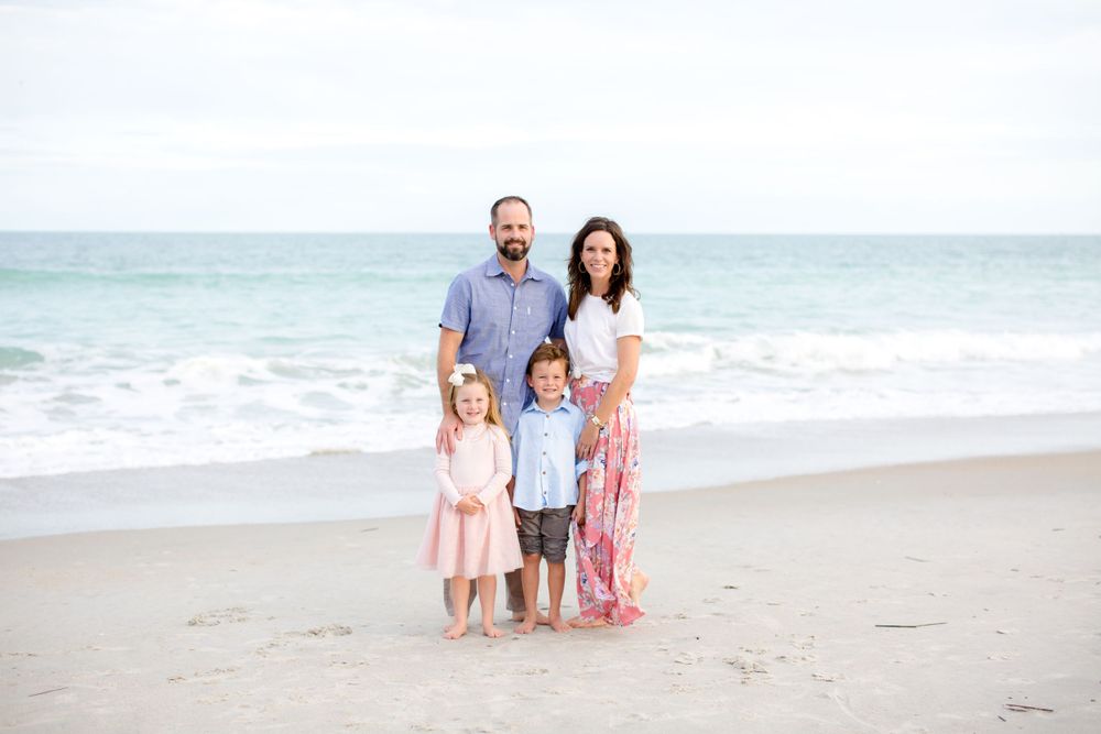 Family of four posing for a portrait on the beach at sunset.