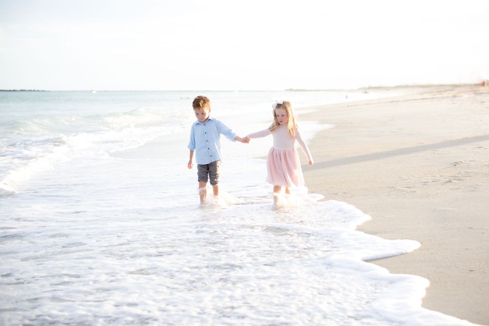 Two children playing in the ocean waves at sunset.