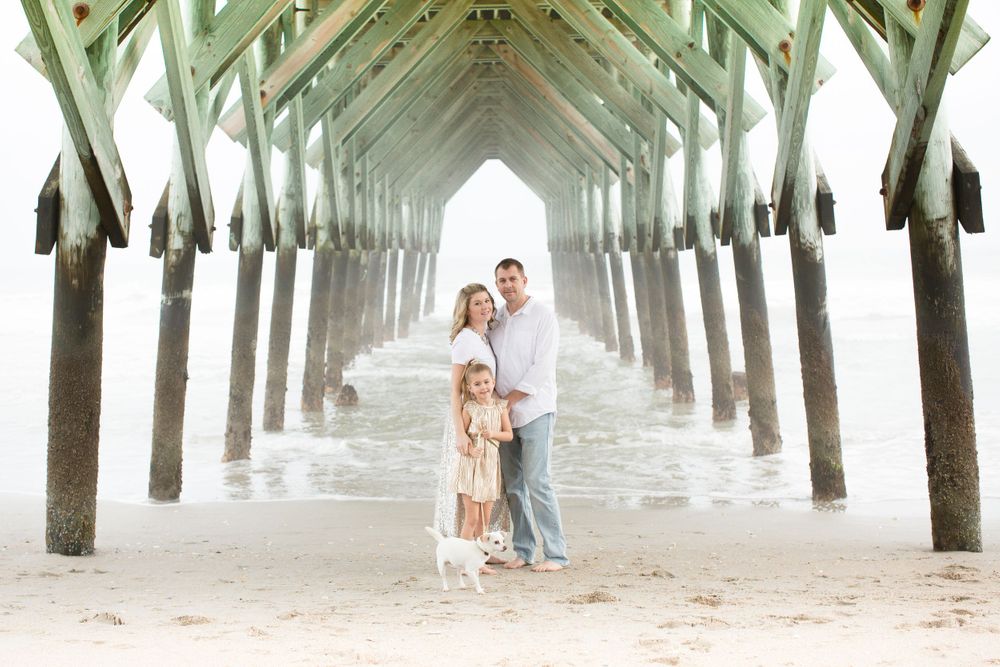 Family portrait under pier supports at beach.