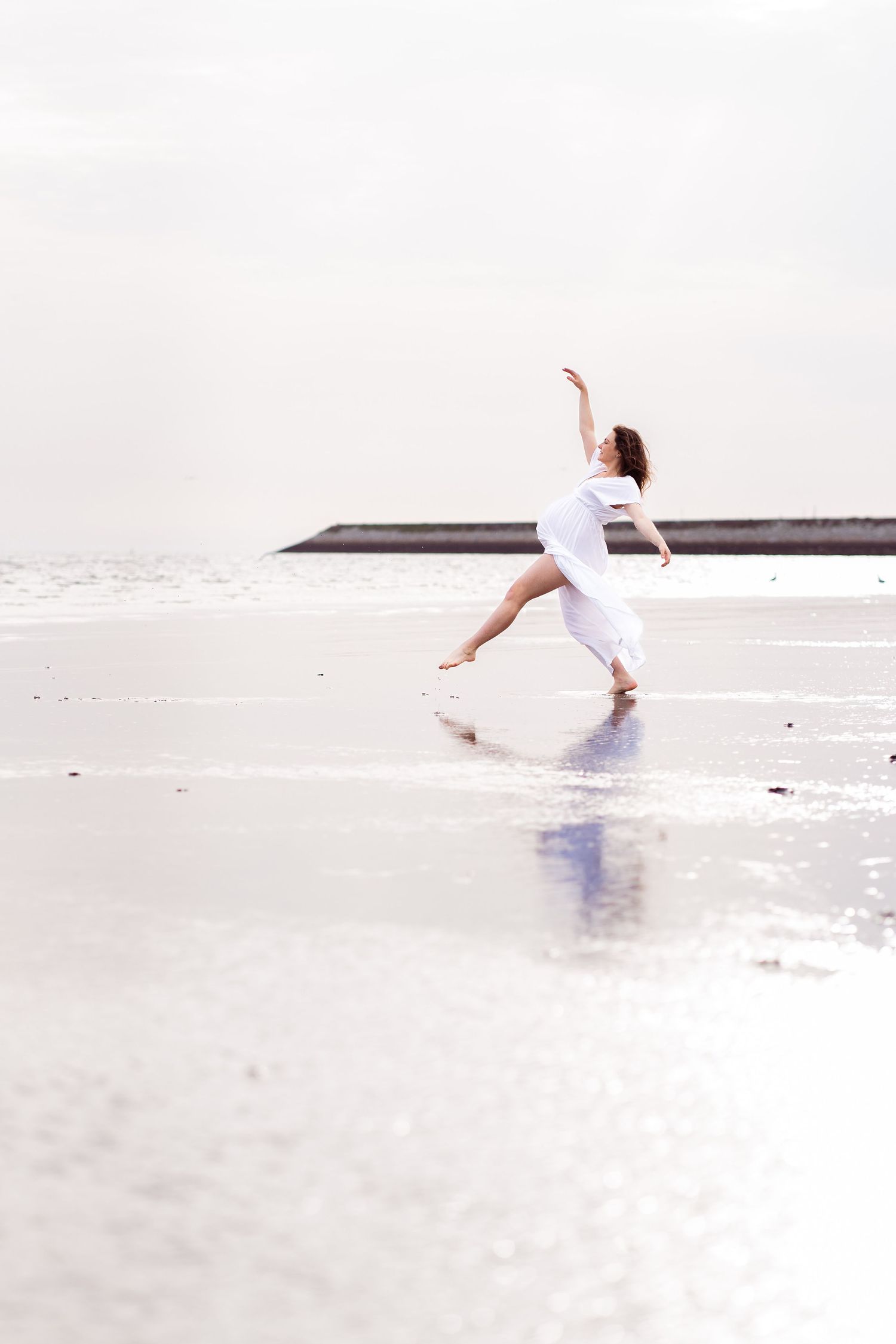 pregnant mom in a white flowy dress dancing ballet on an irish empty beach dublin