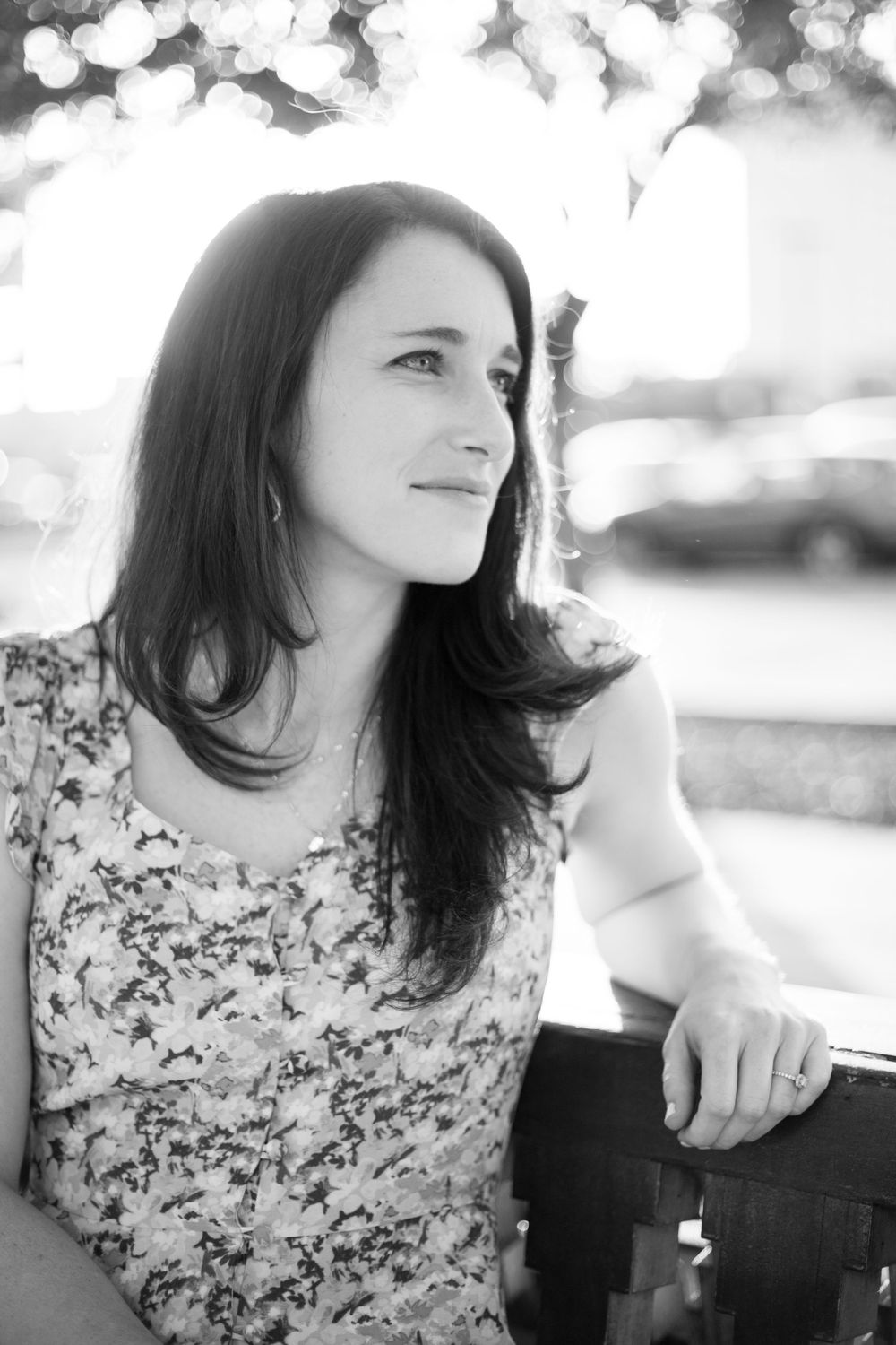 Black and white portrait of brunette woman sitting outdoors with soft bokeh background lighting.