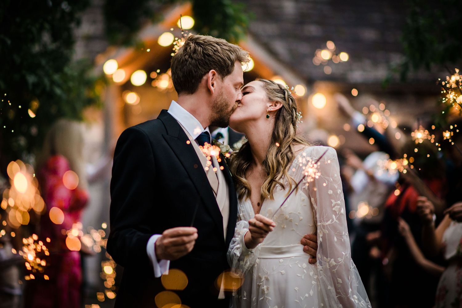 couple in wedding attire kiss whilst surrounded by sparklers at Askham Hall