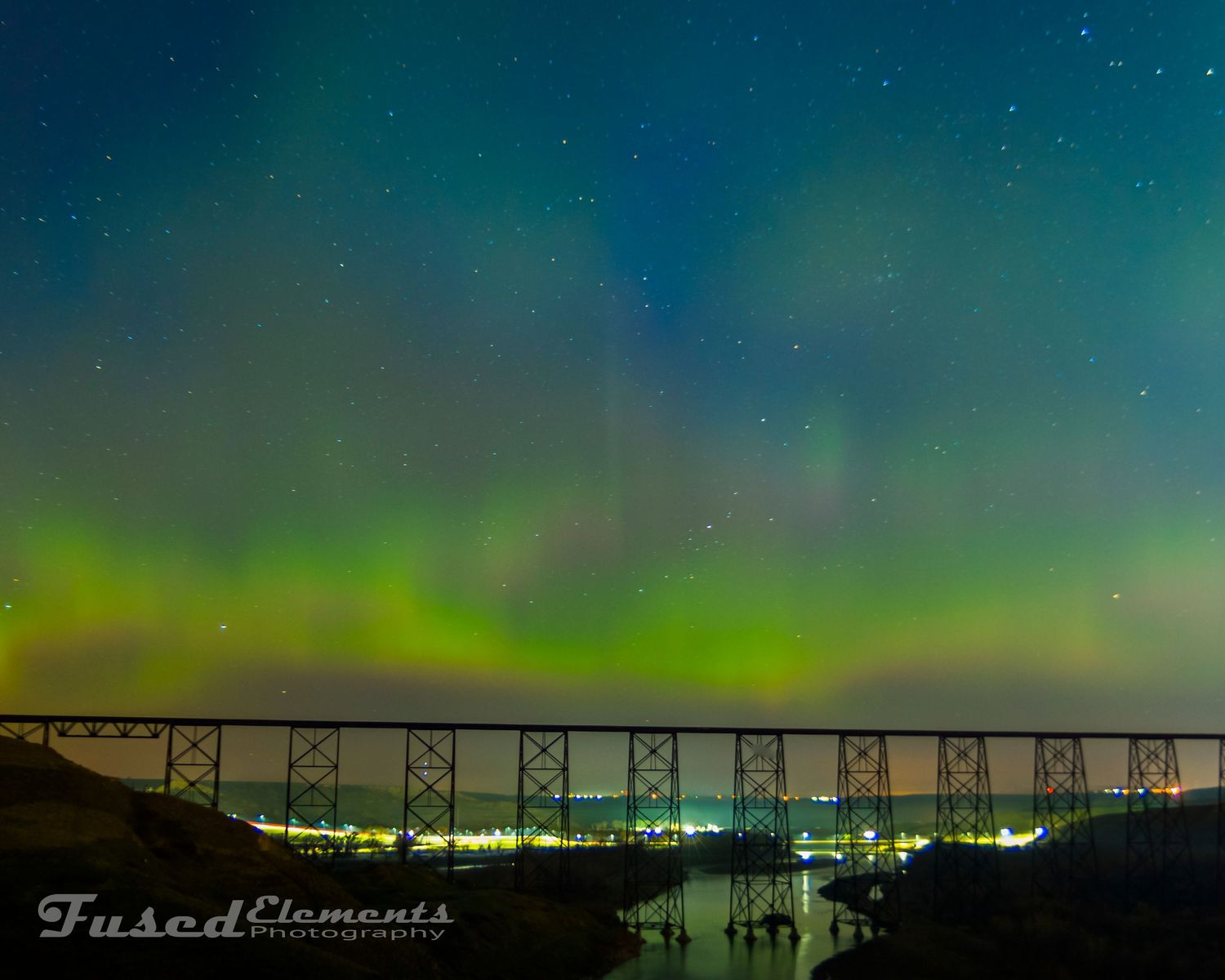 Vibrant green aurora borealis dances across night sky above illuminated bridge spanning dark waters.
