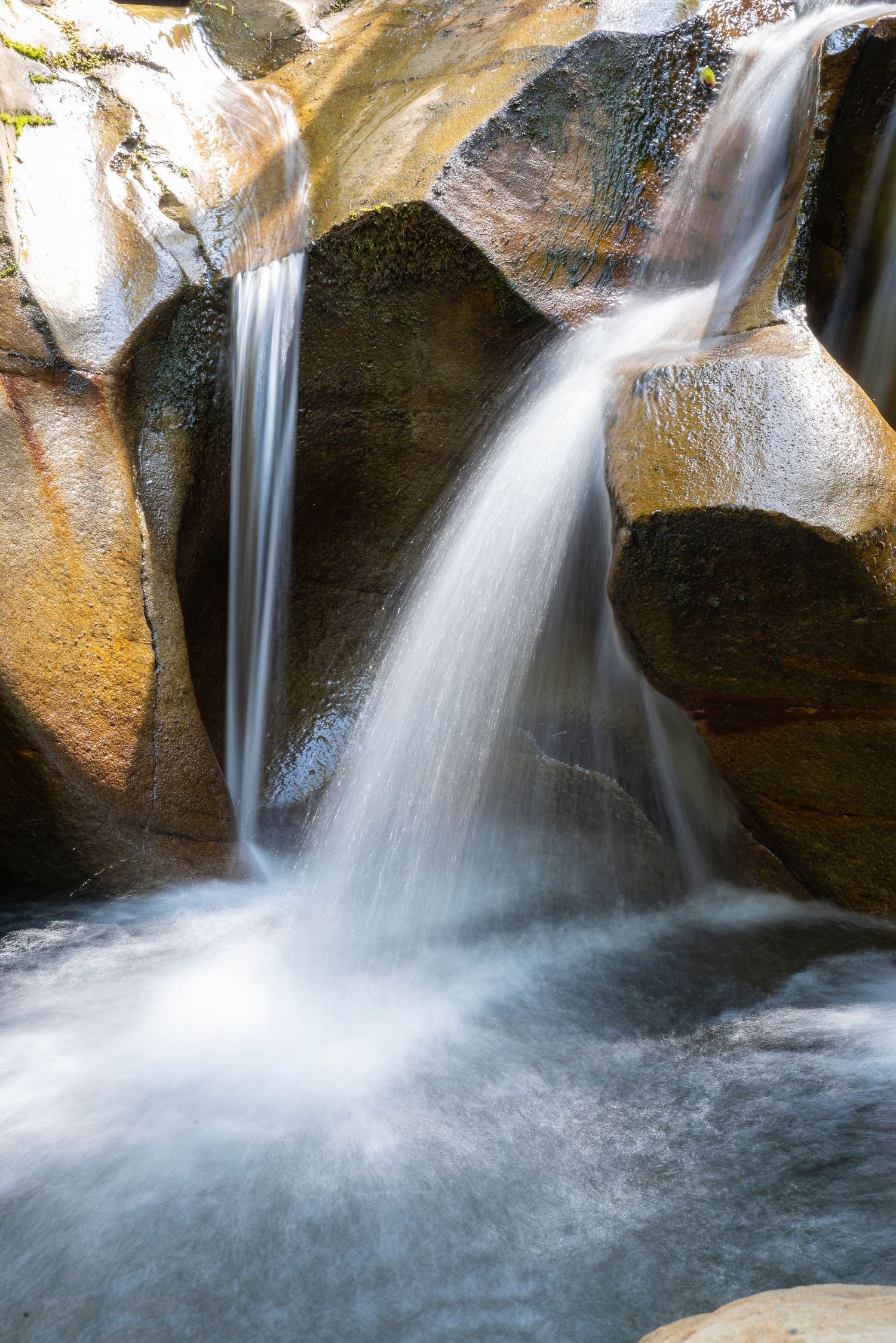 Smooth cascading waterfall flowing over golden-hued granite rocks in close-up detail.