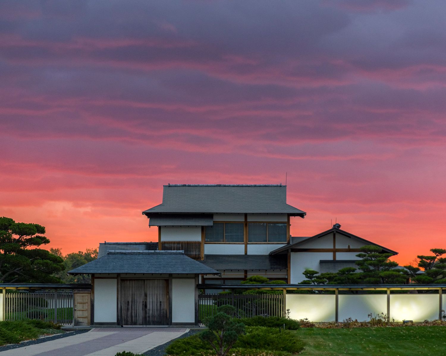Traditional Japanese house glows beneath dramatic pink and purple sunset sky.