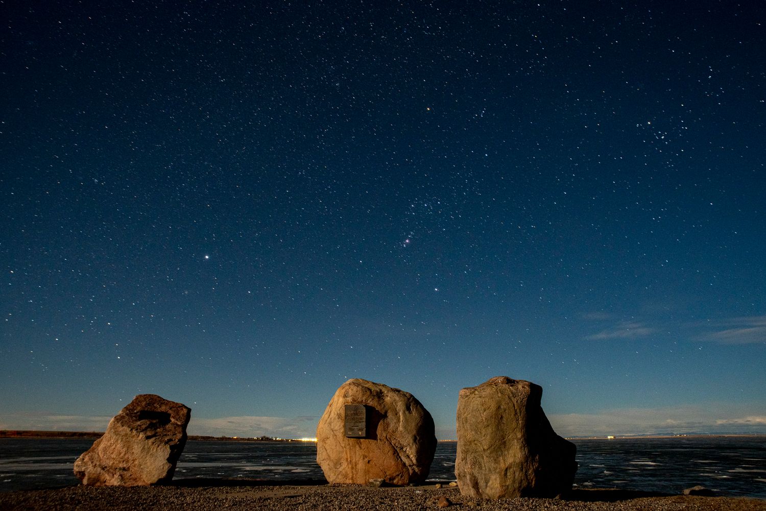 Large boulders silhouetted against starry night sky at coastal location.