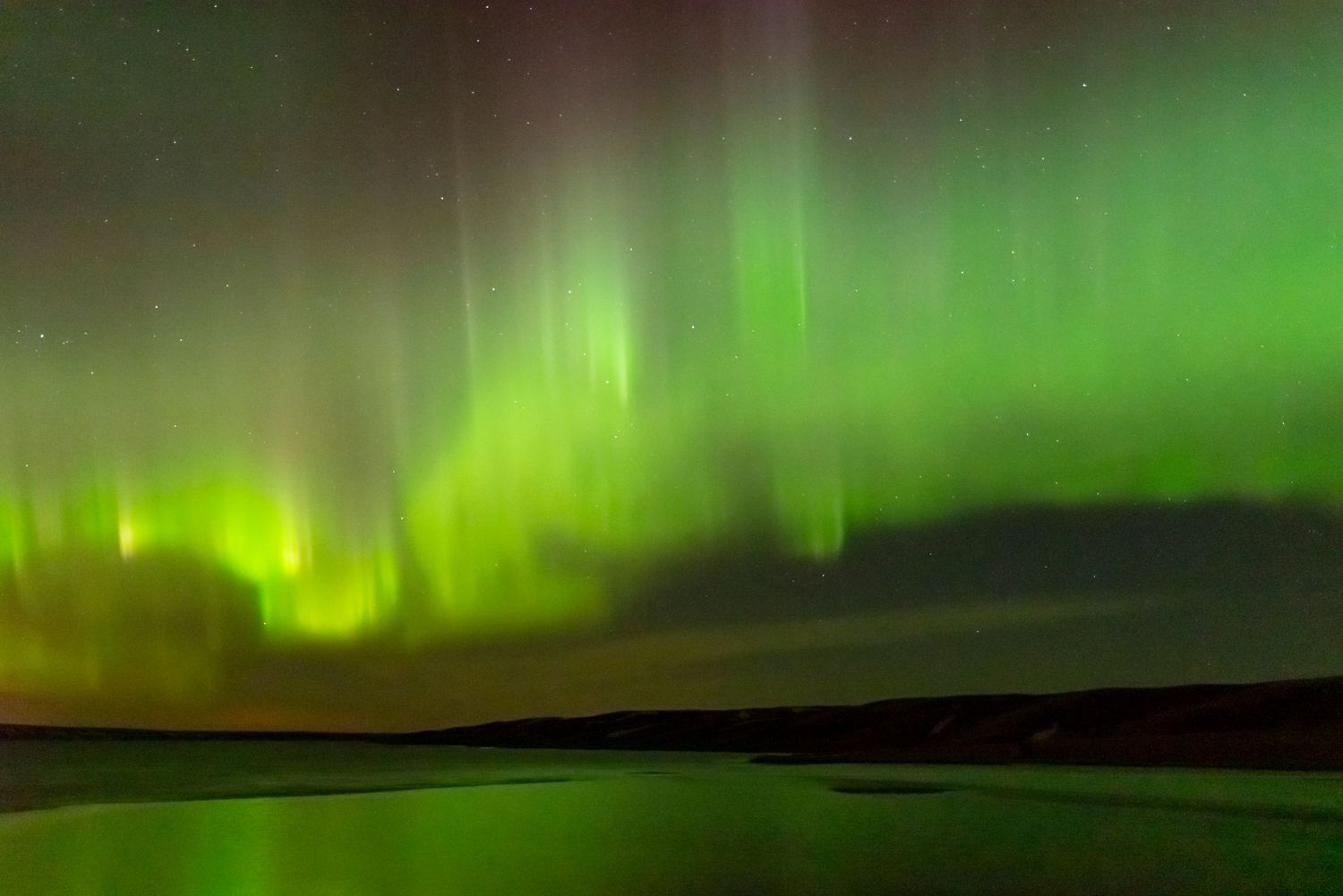 Vibrant green northern lights dance across the night sky over a dark landscape.