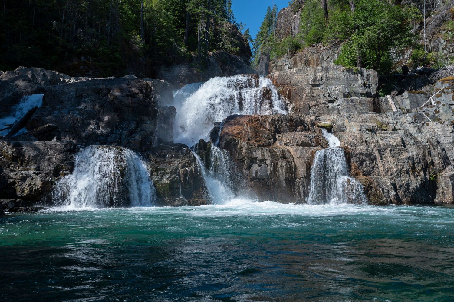 Cascading waterfall flowing over rocky cliffs into turquoise pool.
