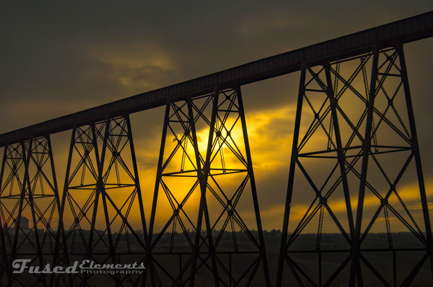 Railroad trestle bridge silhouetted against golden sunset sky with dramatic lighting.