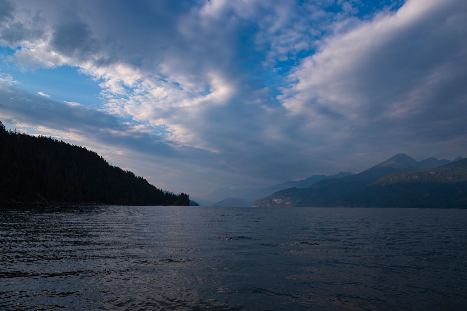Dramatic cloudy sky over a mountain-ringed lake during blue hour.