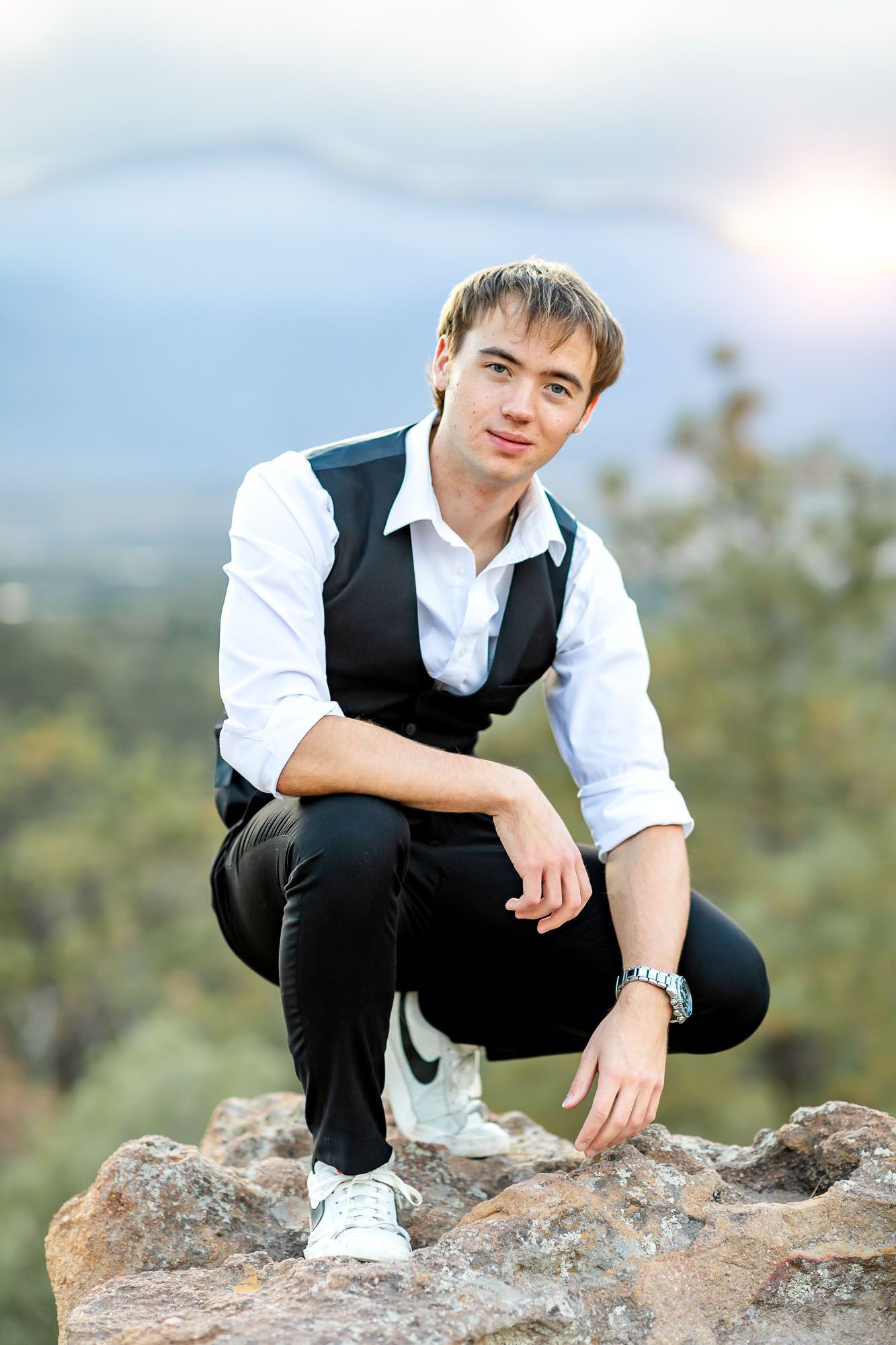 Senior guy smiles softly while squatting on the rocks at his senior session at Palmer Park in Colorado Springs.