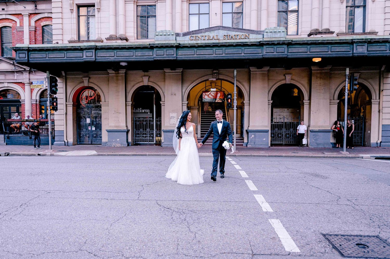 Wedding couple posing in front of historic building with arched walkways and street markings.