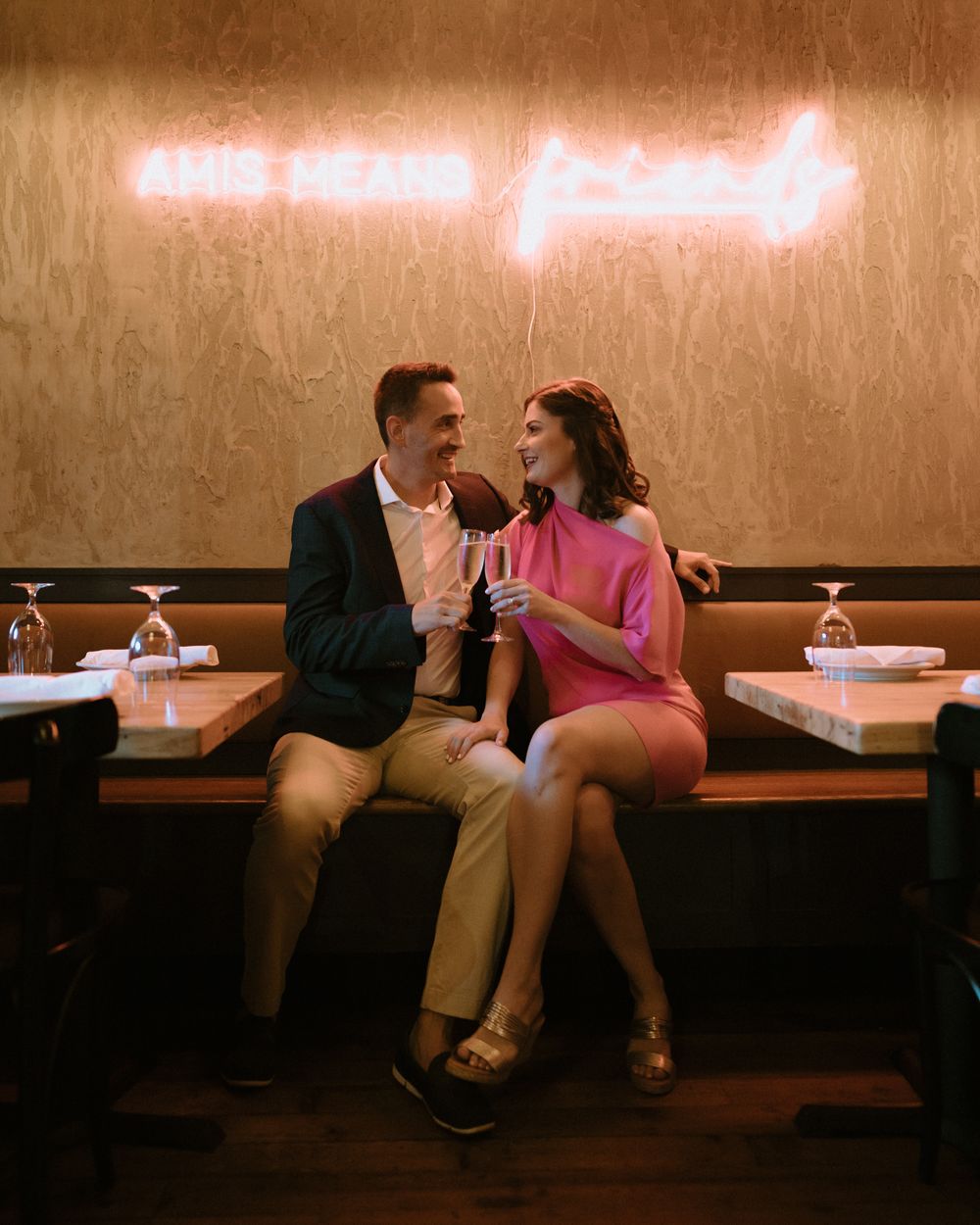 A romantic date night scene with neon lighting as a couple shares drinks at a restaurant booth.