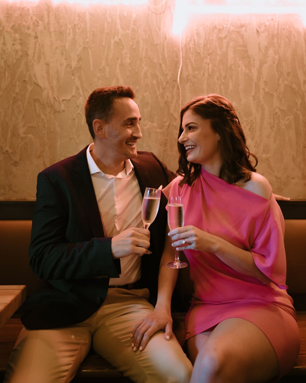 A couple laughs together while sharing champagne at a stylish restaurant with warm lighting.