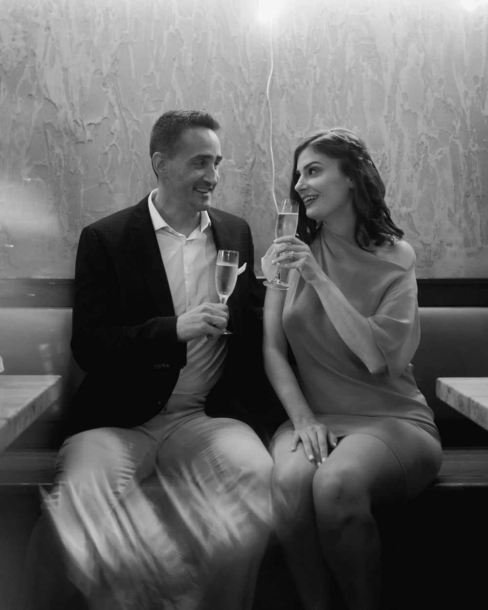 A couple shares an intimate moment while enjoying champagne on a leather booth in a dimly lit venue.