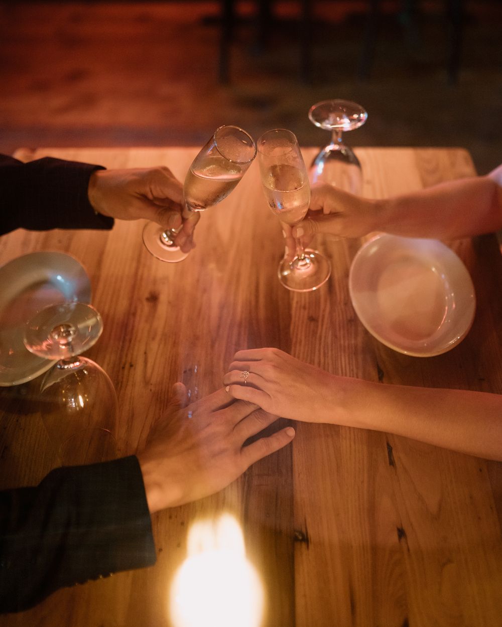 Hands reaching across a wooden table with wine glasses in an intimate dining setting.