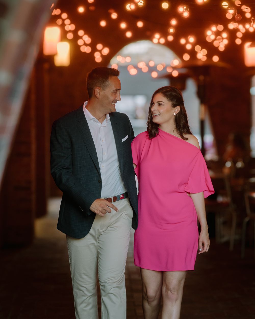 Stylish couple walking together under lit archway in evening attire.