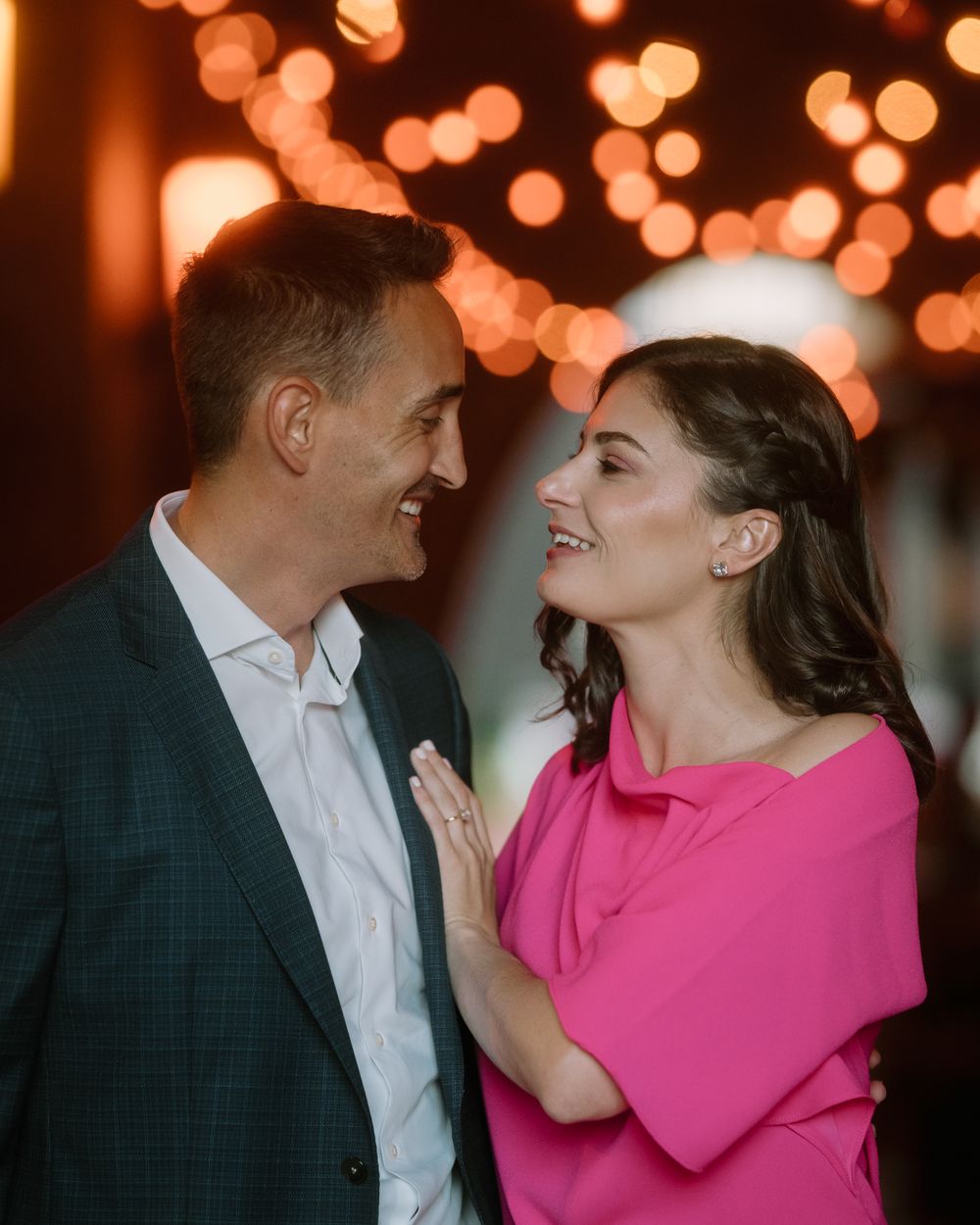 Couple in pink dress and dark suit sharing intimate moment against glowing lights.