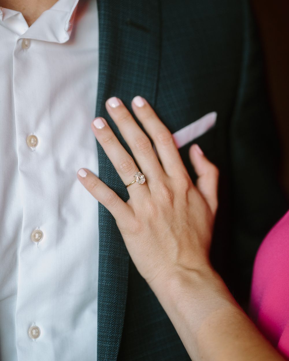 Close-up of hand with engagement ring resting on dark suit jacket and white shirt.