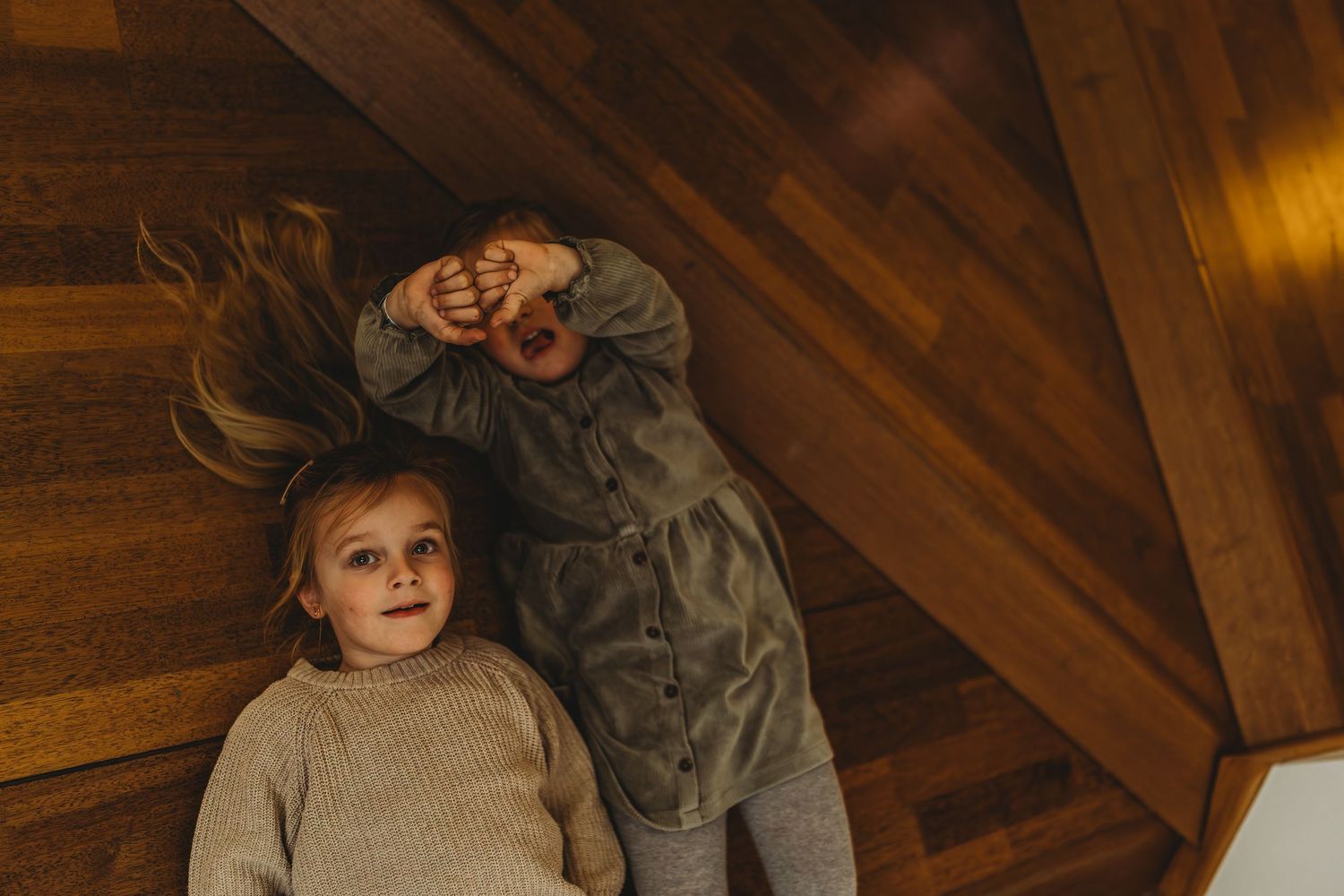Two figures lay on wooden floor boards in a cozy attic space.