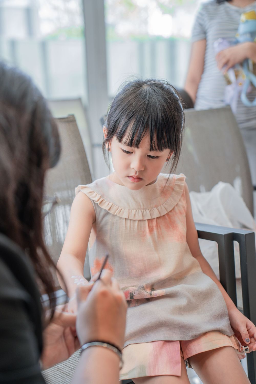 Young girl in peach dress sitting quietly during celebration.