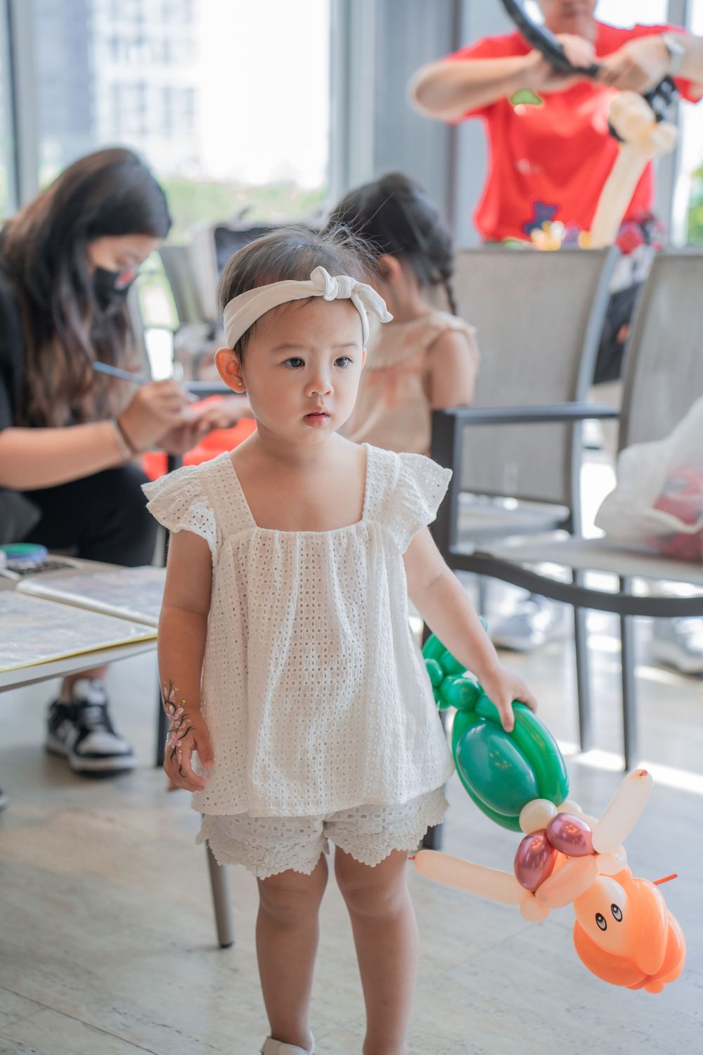 Small child in white dress holding balloon animals at a birthday party.