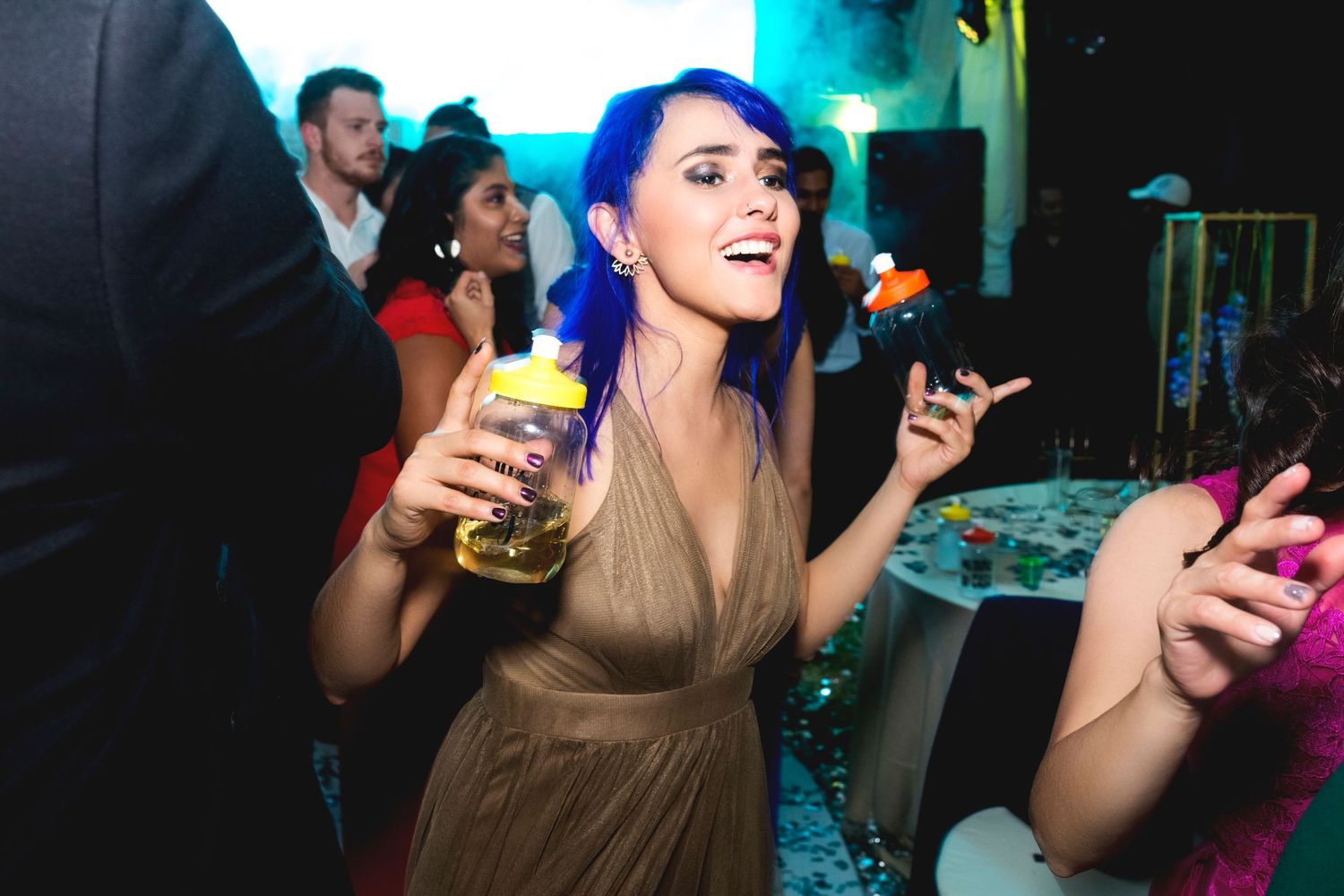 Party guest in a beige dress holding a yellow cocktail while dancing at a nightclub celebration.