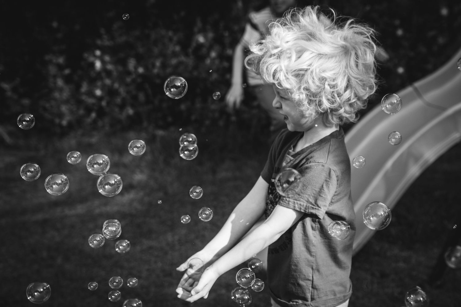 Black and white photo of a child playing with soap bubbles floating in the air.
