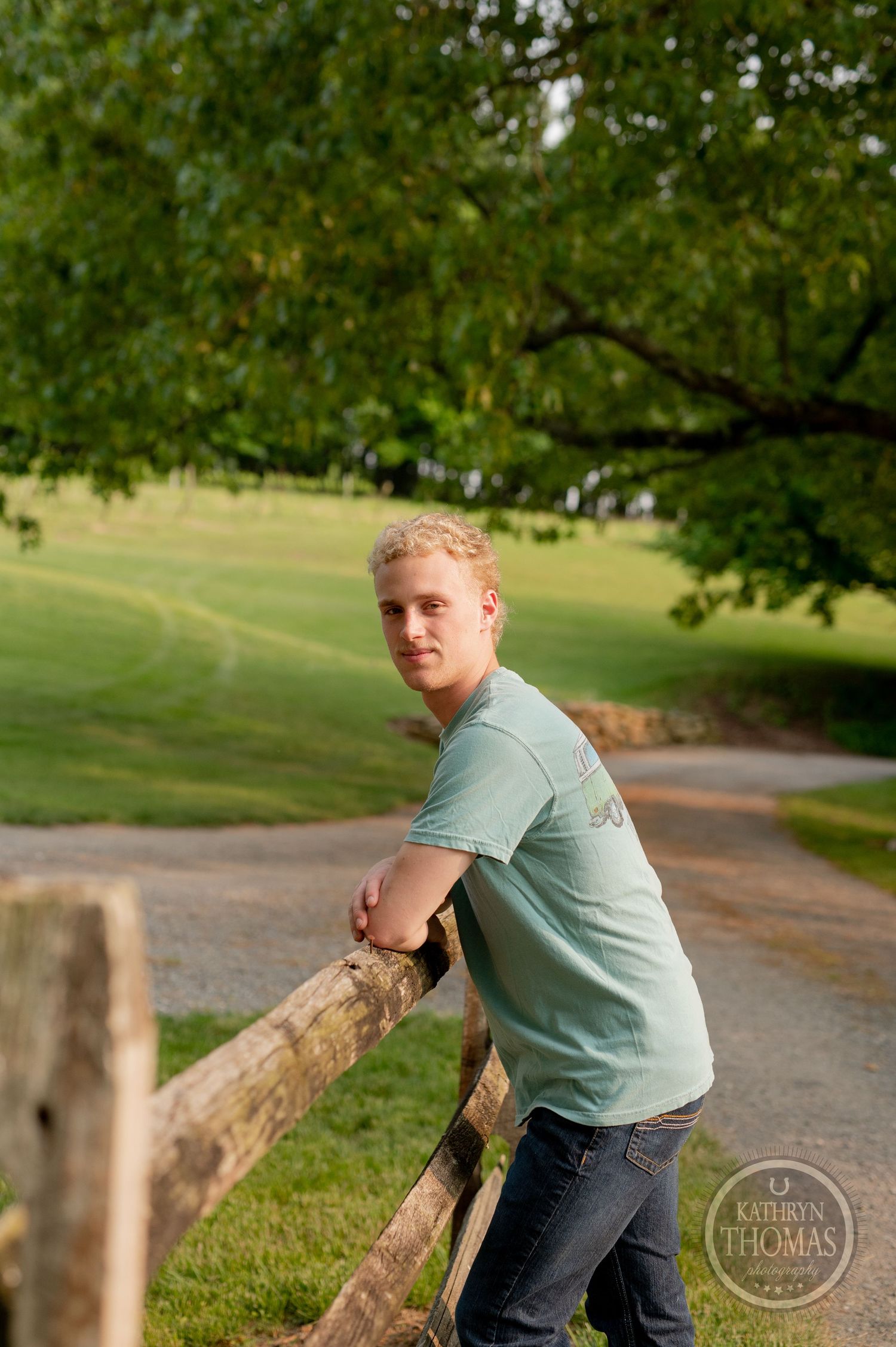 A casual portrait against a wooden fence with trees and rolling hills in the background.