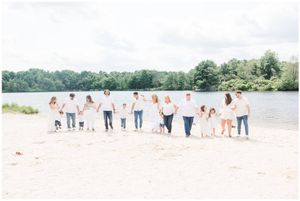 A group of people in light colored clothing stand together on a beach beside a lake.