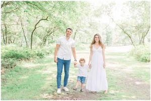 A small group stands together on a sunlit wooded path wearing coordinated white outfits.