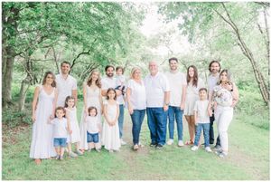 Extended group in white and light colored clothing poses together in a lush green outdoor setting.