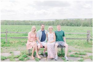 A group sits together on a rustic wooden bench along a gravel path surrounded by green fields.