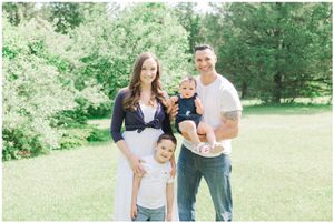 Outdoor family portrait with coordinating navy and white outfits against a green background.