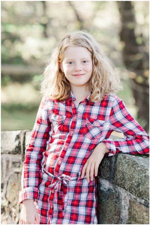 Young person in plaid shirt leans against stone wall outdoors.