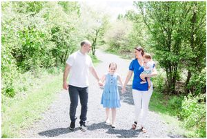 Family walks together holding hands on tree-lined gravel path.