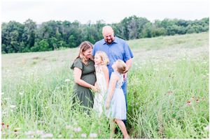Family shares a candid moment together in tall grass field on sunny day.