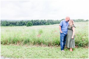 A couple shares an intimate moment while standing in a lush green meadow.