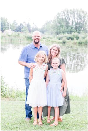 A family of four poses together by a serene lake on a bright summer day.