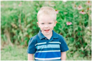 A cheerful little one wearing a blue and white striped polo shirt poses in a garden with flowers.