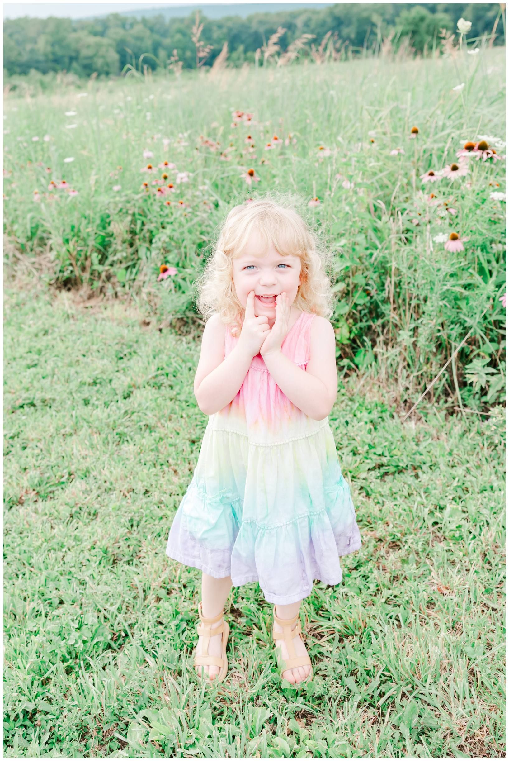 Young child in pastel dress laughs joyfully in wildflower field.