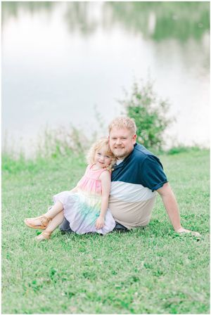 Parent and child share loving moment while relaxing on grassy hill.