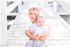 Two children in white shirts pose together on a bright wooden boardwalk.