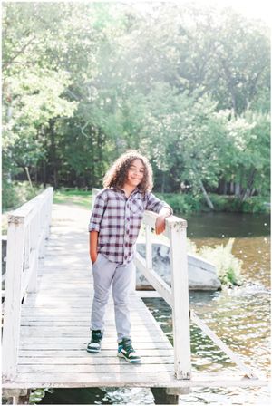 Person wearing plaid shirt and gray pants stands on wooden dock by water.