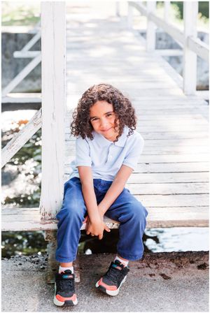 A child in blue jeans and light shirt sits casually on a white wooden deck.