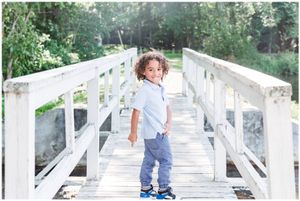 Small child with curly hair stands on white wooden bridge wearing blue shoes.