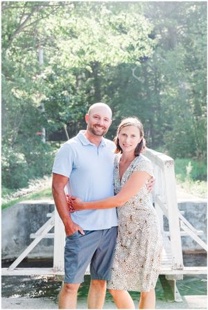 Couple poses together on wooden bridge in summer outdoor setting.