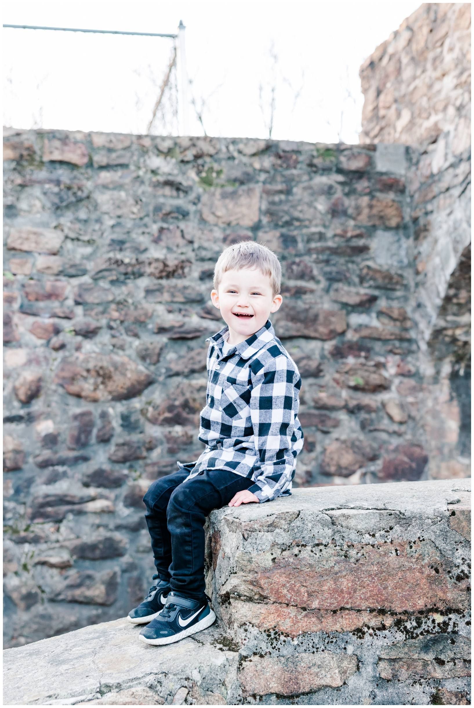 A young child in plaid sits smiling on stone steps outdoors.