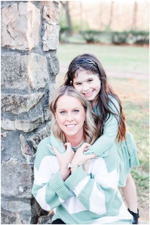 Two people pose together against a stone wall in mint green and white sweaters.